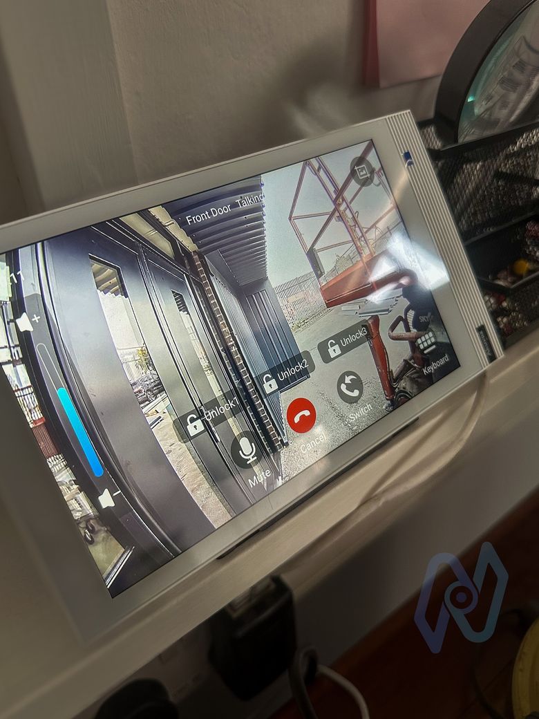 White Akuvox S565 indoor monitor in the office showing the front door camera with unlock buttons