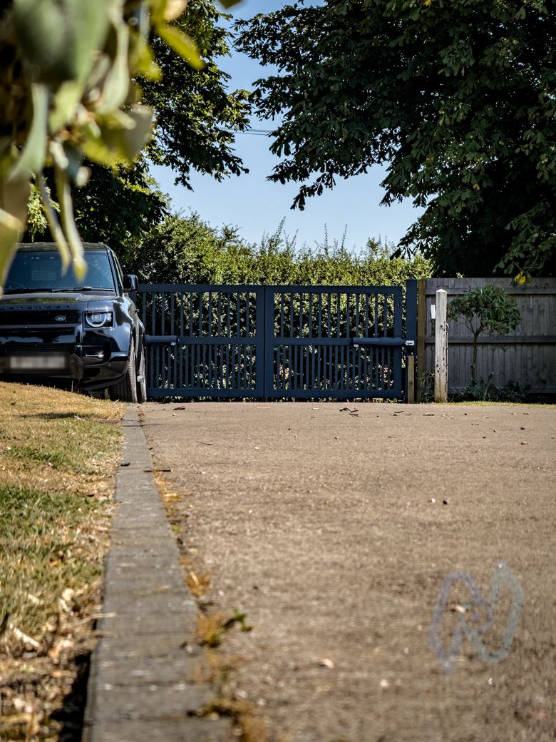 Automated swing gates at the top of the driveway, with a car parked beside them