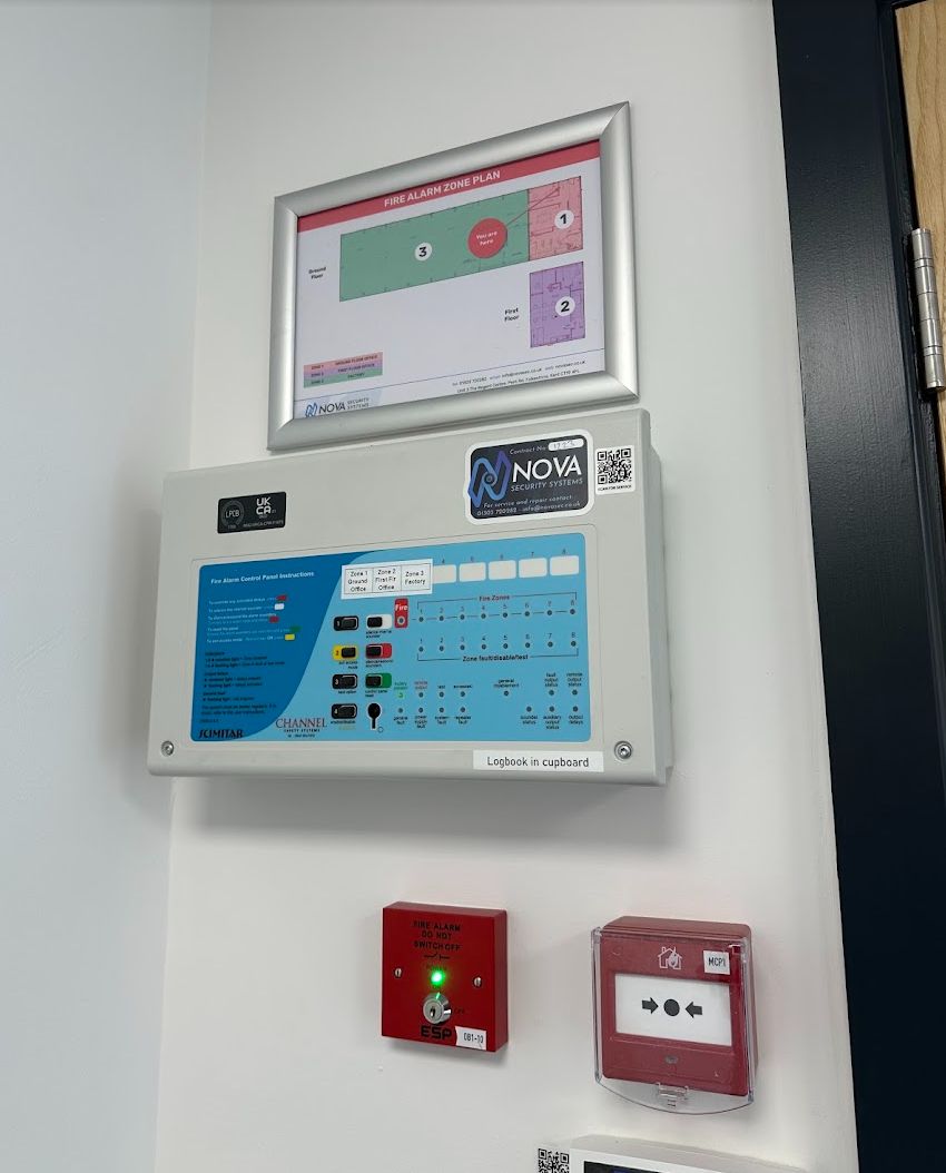 Conventional fire alarm panel with a framed zone plan above it and a Nova service label