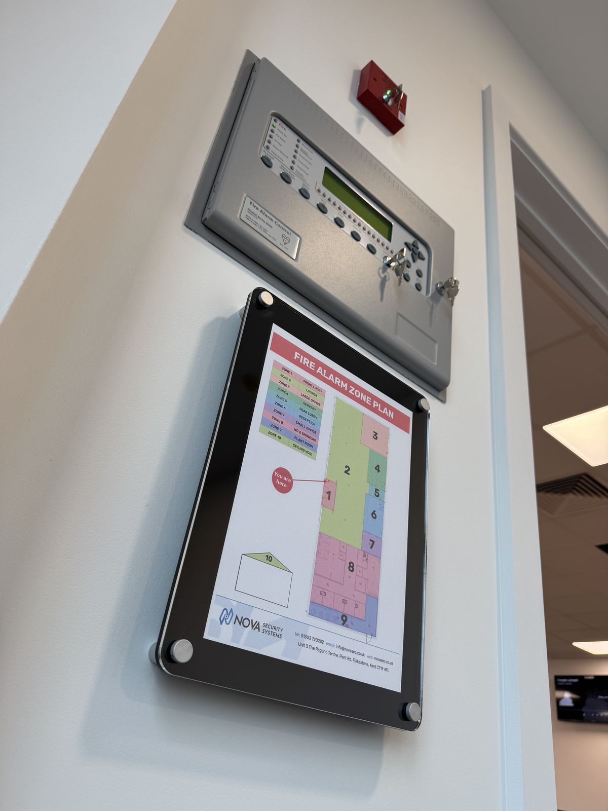 Fire alarm control panel with a framed zone plan mounted beneath it