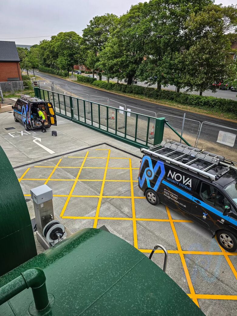 Green cantilever gates and yellow box junction at the Shorncliffe site entrance, with Nova vans