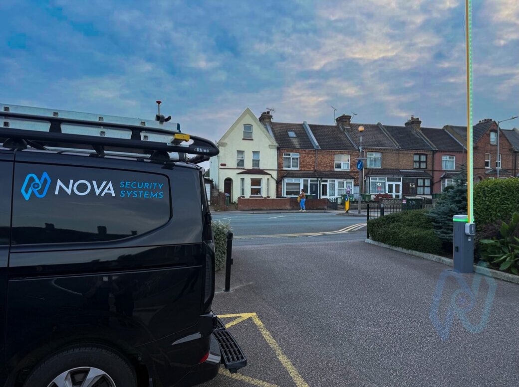 The barrier raised with its boom lit green, beside a Nova van