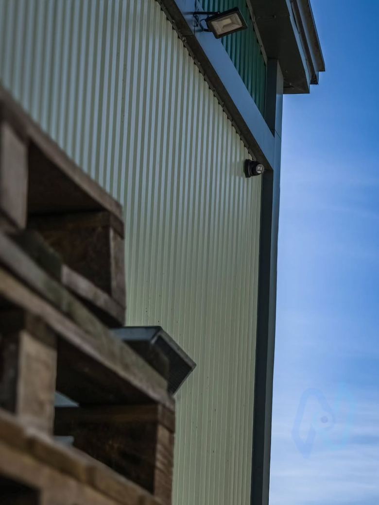 Camera under the eaves of a storage building beside a floodlight
