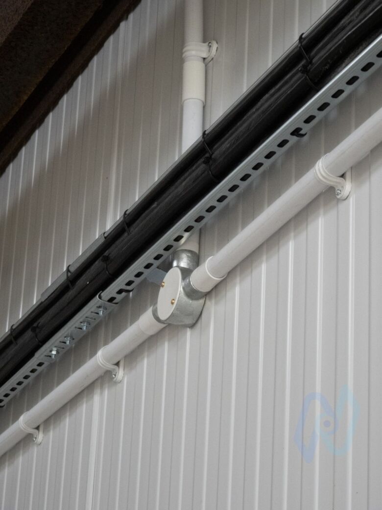 Fire alarm cables in white conduit, run neatly along the workshop’s metal cladding