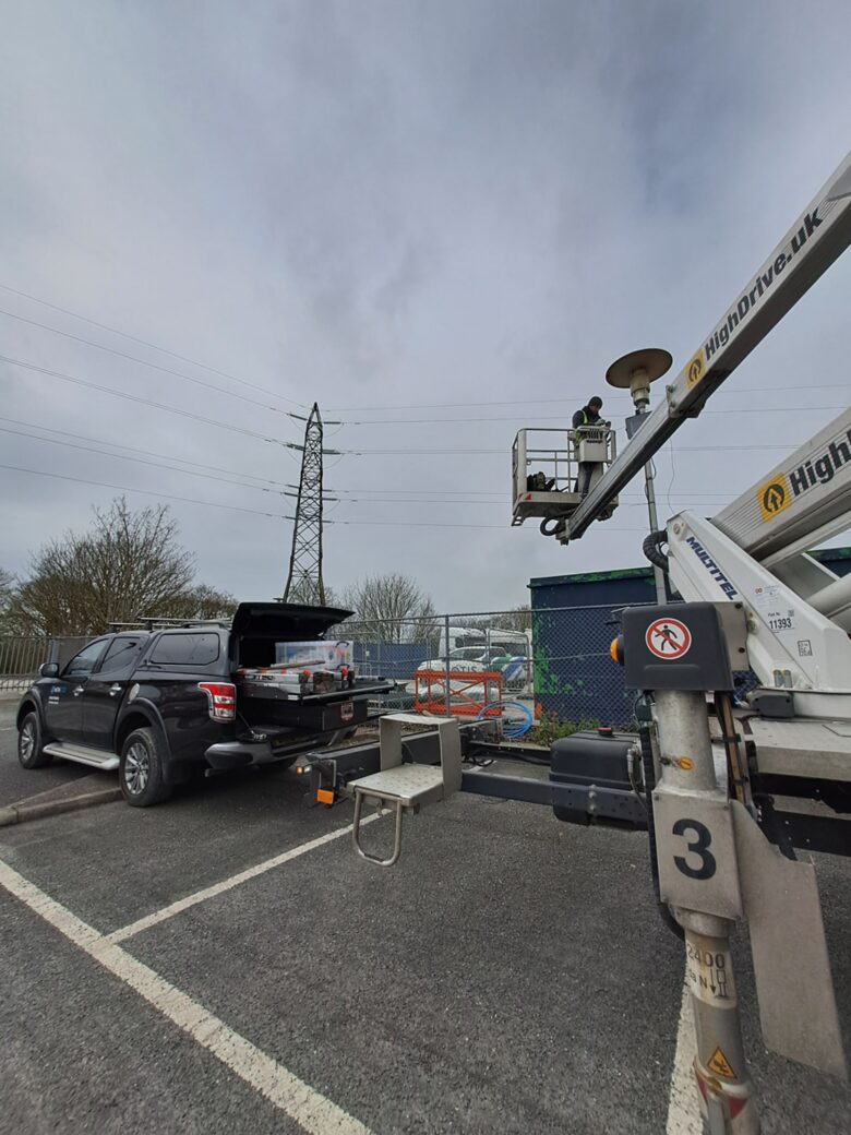 A Nova engineer in the basket of a trailer-mounted boom lift, working at the top of a column