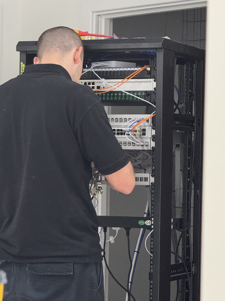 A Nova engineer patching cables in a data cabinet of switches and fibre at Motis Cheriton Truck Park