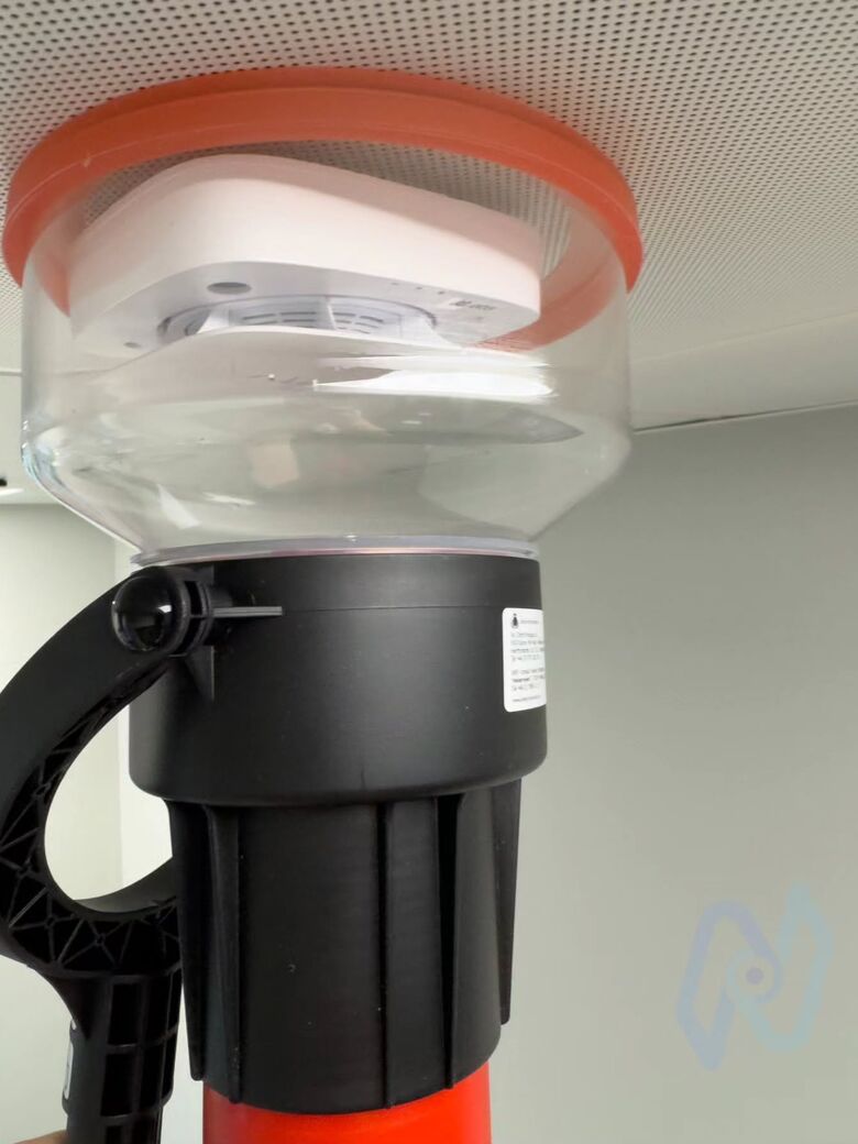 A smoke detector being tested with a smoke tester on a pole