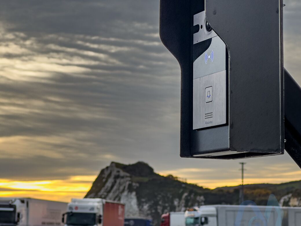 An intercom on a hooded post at Motis Dover, with the white cliffs and parked lorries behind at sunrise