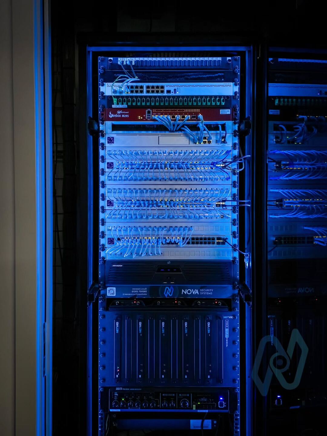 The finished network rack, lit blue, with neatly dressed patch leads and the Nova panel