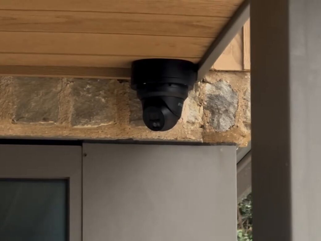 A black CCTV dome camera under the timber soffit of the house