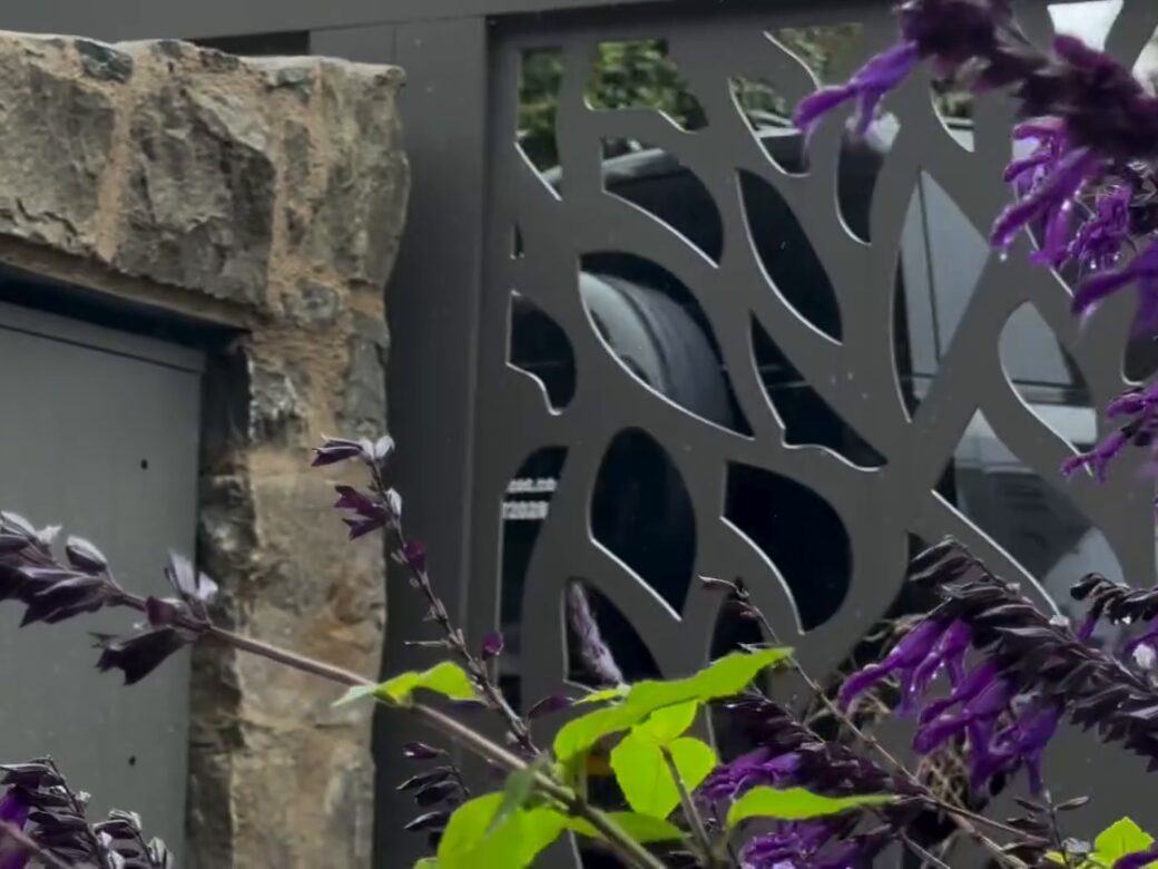 Close-up of the waterjet-cut tree pattern on the gate beside a stone pillar