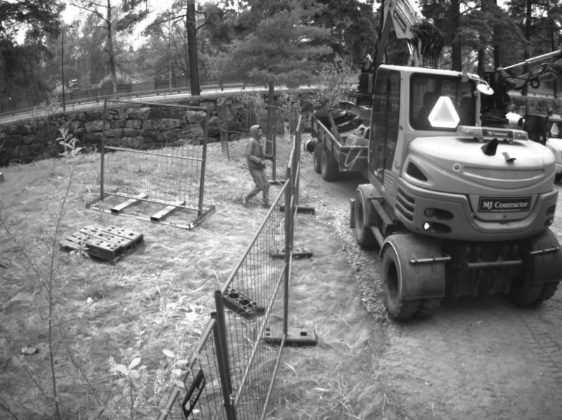 Night-time Reconeyez alarm photo of a person walking past Heras fencing beside an excavator