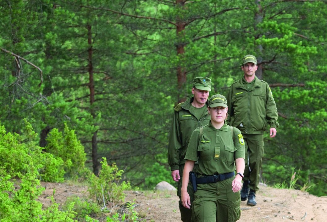 Three border guards in uniform walking through a forest
