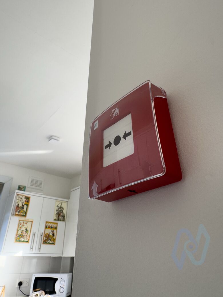 A red Ajax EN54 manual call point with a clear cover in an HMO shared kitchen
