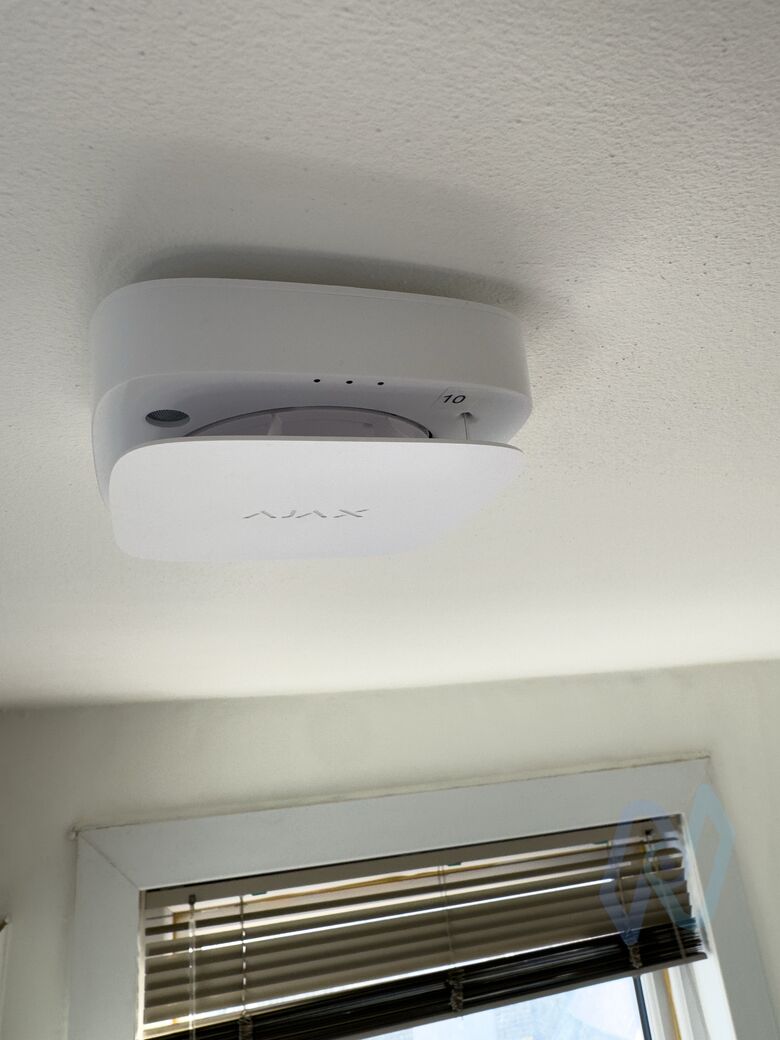 An Ajax EN54 wireless fire detector on a ceiling by a window